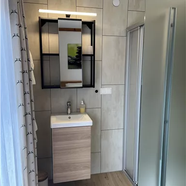 Ein modernes Badezimmer mit einem hellen Waschbecken und einem großen Spiegel. Die Wände sind mit Fliesen verkleidet und eine Glasduschkabine ist vorhanden.