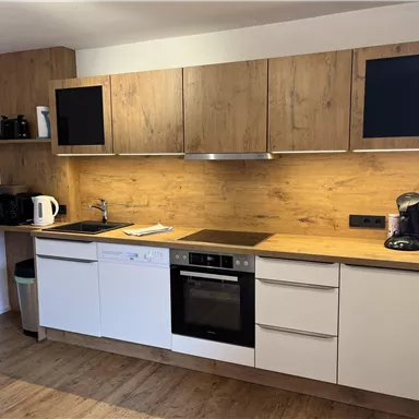 Eine moderne Küche mit Holzregalen und weißen Schränken. Die Ausstattung umfasst einen Wasserkocher, eine Kaffeemaschine und einen Geschirrspüler.