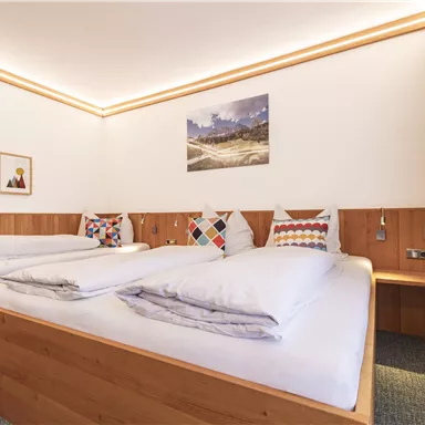 Ein gemütliches Schlafzimmer mit zwei Betten und holzverkleideten Wänden. Die Raumbeleuchtung und ein großes Fenster sorgen für eine angenehme Atmosphäre.