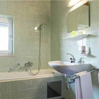 Ein modernes Badezimmer mit mintgrünen Fliesen und natürlichem Licht. Es verfügt über eine Badewanne, ein Waschbecken und eine Dusche.