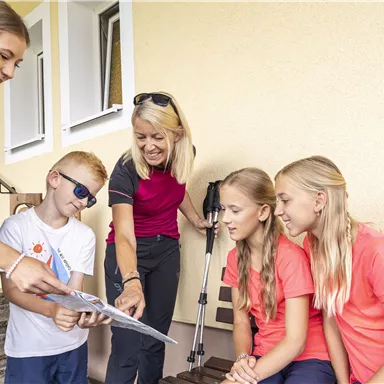 Eine Gruppe von fünf Personen steht vor einem Gebäude und betrachtet einen Stadtplan. Sie scheinen sich auf einen Ausflug oder eine Aktivität vorzubereiten.