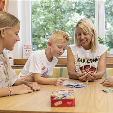 Eine fröhliche Spielrunde mit Kindern und einer Frau am Tisch. Sie spielen mit Karten und wirken entspannt und glücklich.