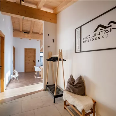 Ein einladender Flur mit hellen Wänden und Holzdetails. Im Raum gibt es eine Garderobe und einen gemütlichen Sessel.