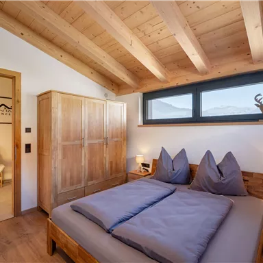 Ein modernes Schlafzimmer mit einer Holzdecke und elegantem Mobiliar. Der Raum ist hell und einladend, mit einem großen Fenster, das den Blick nach draußen freigibt.