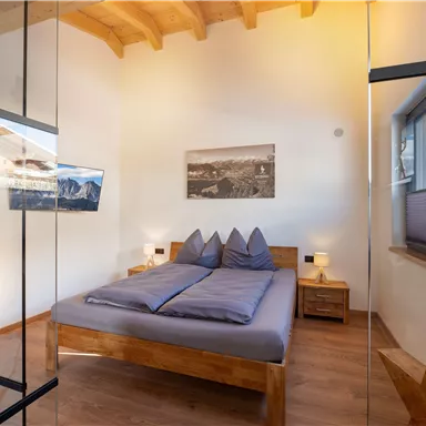 Ein modernes Schlafzimmer mit Holzdetails und großen Fenstern. Das Bett hat graue Bettwäsche und es gibt ein Bild an der Wand.