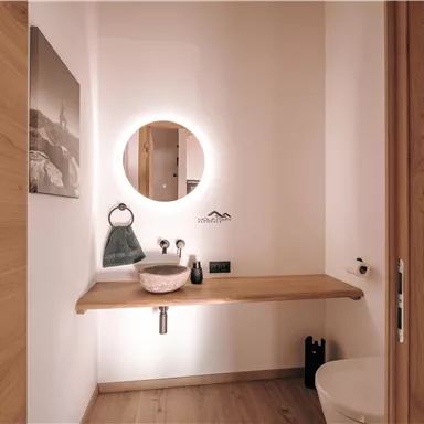 Ein modernes Badezimmer mit einer Holzoberfläche und einer runden Spiegelleuchte. Die Einrichtung ist minimalistisch mit einem Waschbecken und einer toilet.