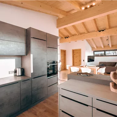 Eine moderne Küche mit Holzdetails und eleganten Möbeln. Der Raum wirkt hell und einladend, mit einem offenen Wohnbereich im Hintergrund.