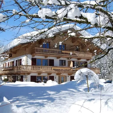 Ein gemütliches Holzhaus im Schnee, umgeben von schneebedeckten Bäumen. Der klare blaue Himmel sorgt für eine festliche Winteratmosphäre.