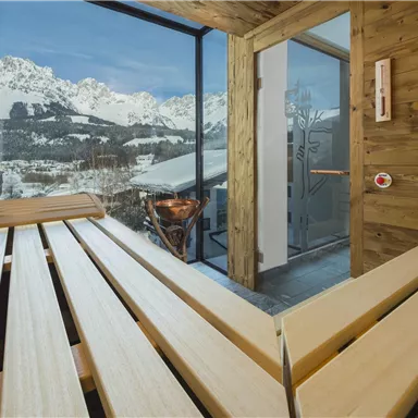 Ein gemütlicher Saunabereich mit Holzliegeflächen und Aussicht auf schneebedeckte Berge. Große Fenster ermöglichen einen Blick auf die beeindruckende Natur.