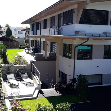 Ein modernes Gebäude mit Balkon und großzügiger Terrasse. Der Garten ist gepflegt und mit Liegen und Pflanzen ausgestattet.