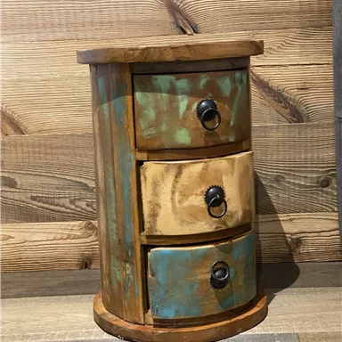 A round wooden table with three drawers in different colors. It has a rustic look and stands in front of a wooden panel.