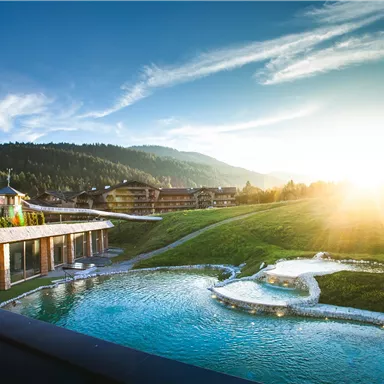 A picturesque landscape with an adjacent pond and gentle hills. The sun rises over the mountains, creating a peaceful atmosphere.