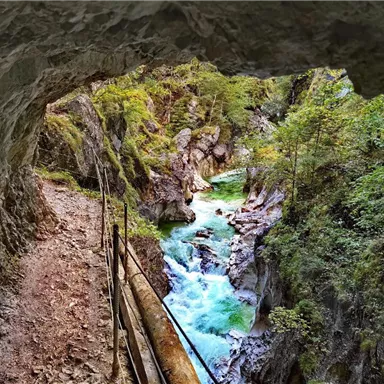 Ein Blick aus einer Höhle auf einen klaren, türkisfarbenen Fluss, der durch eine felsige Schlucht fließt. Umgeben von üppigem Grün und Schieferfelsen ist die Landschaft atemberaubend.