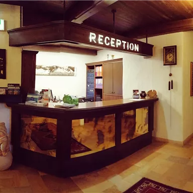 Ein einladender Empfangsbereich mit einer Holztheke und warmem Licht. An den Wänden sind dekorative Bilder und Informationen für Gäste angebracht.