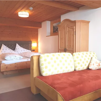 Ein gemütliches Schlafzimmer mit einem Doppelbett und einem Holzschrank. Eine bequeme Couch mit bunten Kissen ergänzt die einladende Atmosphäre.