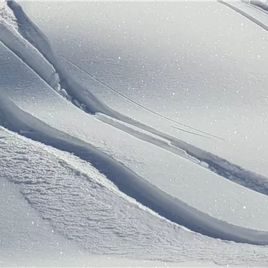 A gentle snow hill with delicate waves and sparkling crystals. The white lines show the traces in the fresh snow.