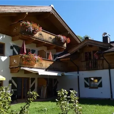 Ein charmantes Haus im alpinen Stil mit einem schönen Garten und Balkonen. Die Fassade ist in hellen Farben gehalten, umgeben von natürlicher Vegetation.