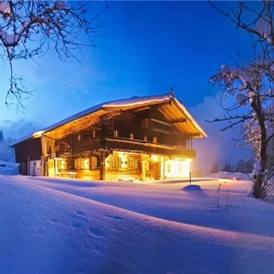 A beautiful chalet in a snowy winter landscape. The warm light radiates from the windows, creating a cozy atmosphere.