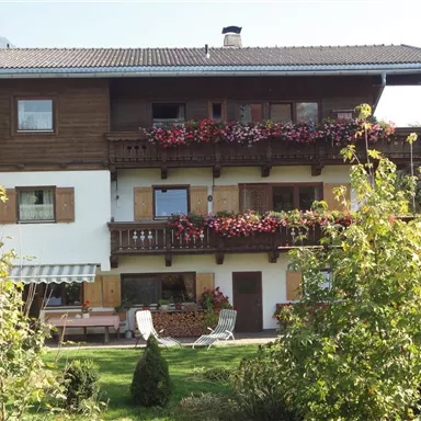 Ein gemütliches Haus im alpinen Stil mit blühenden Balkonen. Der Garten ist grün und einladend, ideal zum Entspannen.
