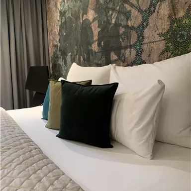 A modern bedroom with a large bed and colorful pillows. The wall is decorated with an artistic pattern.