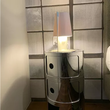 A modern bedside table made of glossy material with three drawers. On top is a stylish lamp with a colored lampshade.