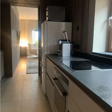 A modern kitchen with bright colors and a cooktop. In the background, a cozy living area is visible.