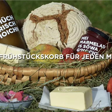 Ein Frühstückskorb mit frischen Zutaten wie Brot, Butter, Marmelade und Obst. Die Produkte sind liebevoll arrangiert und laden zum Genießen ein.