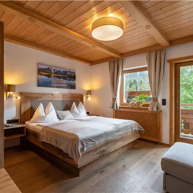 Ein gemütliches Schlafzimmer mit einem Doppelbett und Holzdecke. Der Raum hat große Fenster, die viel natürliches Licht hereinlassen.