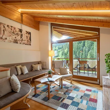 Ein gemütliches Wohnzimmer mit modernem Holzdesign und großen Fenstern. Der Raum ist hell erleuchtet und bietet einen Blick auf eine grün bewachsene Landschaft.