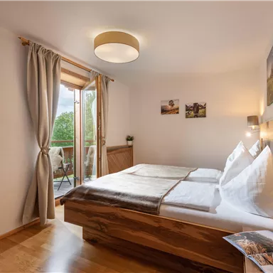 Ein gemütliches Schlafzimmer mit zwei Betten und natürlichem Holzdekor. Große Fenster sorgen für viel Tageslicht und bieten einen Blick ins Freie.