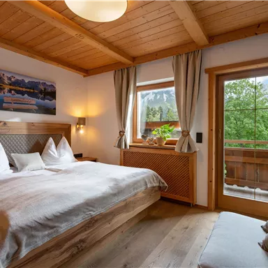 Ein gemütliches Schlafzimmer mit einem großen Doppelbett und Holzmöbeln. Das Fenster bietet einen Blick auf die grüne Landschaft außerhalb.