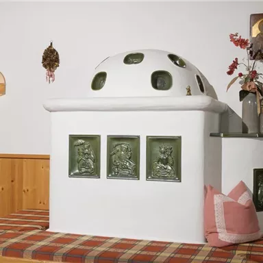 A cozy fireplace with a round dome and decorative reliefs. Next to it is a cushioned bench with pillows in red and pink.