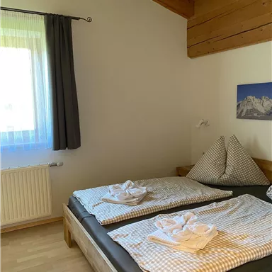 Ein gemütliches Schlafzimmer mit zwei Betten und Holzdecken. Die Fenster lassen viel Tageslicht herein, und die Atmosphäre ist einladend.