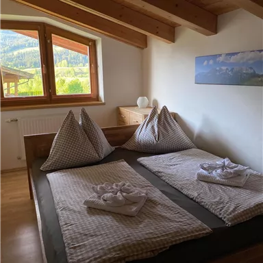 Ein gemütliches Schlafzimmer mit einem Doppelbett und zwei großen Kopfkissen. Die Fenster bieten einen Blick auf die umliegende Natur.