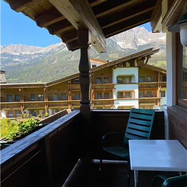 Ein Balkon mit Blick auf die Berge und eine gemütliche Sitzgelegenheit. Die Umgebung ist von Holzarchitektur und grünen Pflanzen geprägt.