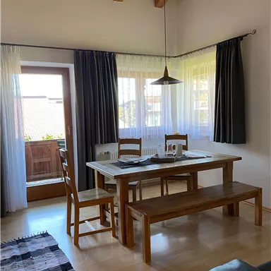 Ein helle, einladende Esszimmer mit einem Holztisch und Stühlen. Große Fenster sorgen für viel Tageslicht und eine angenehme Atmosphäre.