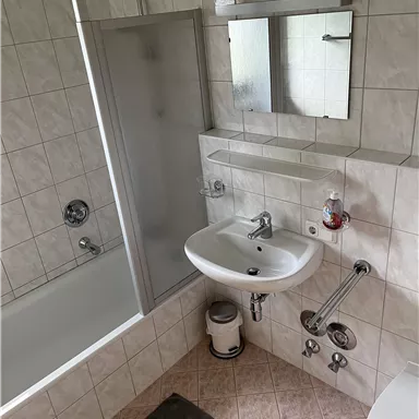 Ein modernes Badezimmer mit einer Dusche, Badewanne und Waschbecken. Die Wände sind gefliest und es gibt einen großen Spiegel.