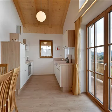 Eine moderne Küche mit Holzmöbeln und großen Fenstern. Der Raum hat viel Tageslicht und bietet einen Blick auf die Landschaft.