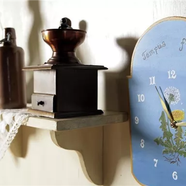 Ein rustikaler Holzregal mit einer Kaffeekanne und einer alten Kaffeemühle. An der Wand hängt eine blaue Wanduhr mit dem Schriftzug "Tempus fugit".