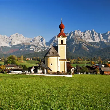 Eine malerische Kirche in der Landschaft mit Bergen im Hintergrund. Grüne Wiesen umgeben die attraktive Szenerie.