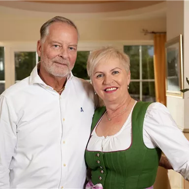 A couple smiles in an elegant living space. The woman is wearing a traditional dress and the man is in a white shirt.