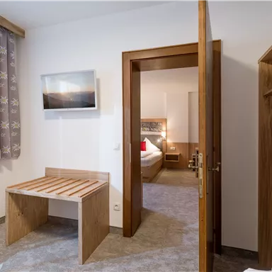 Ein gemütliches Zimmer mit einem Holztisch und einem Stuhl. Im Hintergrund ist ein weiteres Zimmer sichtbar, das modern eingerichtet ist.