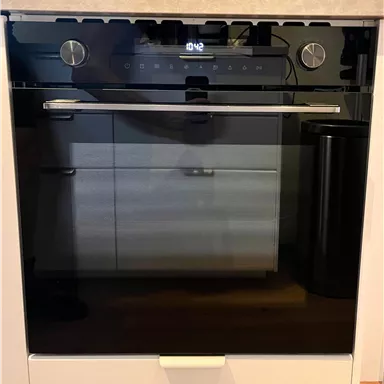Ein moderner Backofen mit einem schwarzen Glasfront und digitalen Bedienelementen. Er befindet sich in einer hellen Küchenumgebung.