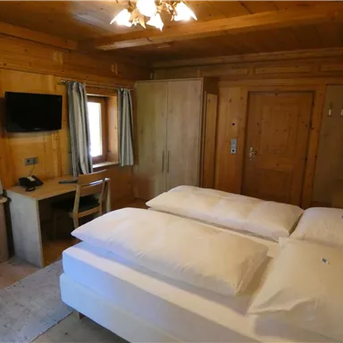 Ein gemütliches Schlafzimmer mit Holzverkleidung und zwei einzelnen Betten. Es gibt einen kleinen Schreibtisch und einen Fernseher an der Wand.