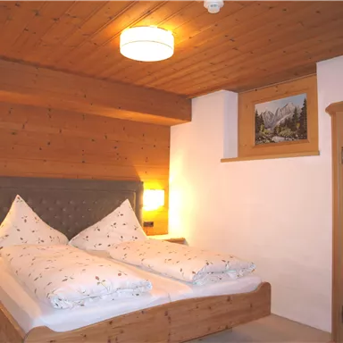 Ein gemütliches Schlafzimmer mit einem Doppelbett und holzverkleideten Wänden. Das Zimmer hat warmes Licht und eine malerische Wanddekoration.