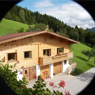 A charming wooden house in the mountains, surrounded by green meadows and trees. The architecture is traditional and inviting.
