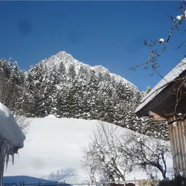 A snowy landscape with high mountains in the background. The sun shines over the snow-covered huts and the tranquil scenery.