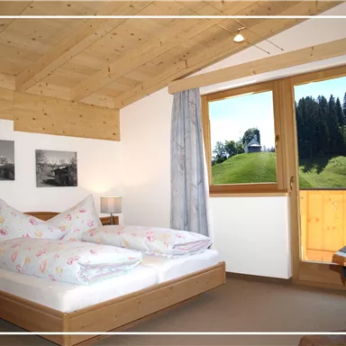 Ein gemütliches Schlafzimmer mit einem Doppelbett und Holzdecke. Der Blick aus dem Fenster zeigt eine grüne Landschaft mit Bäumen.