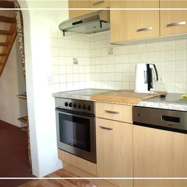 Eine moderne Küche mit Holzschränken, einem Herd und einer Spüle. Im Hintergrund ist eine Treppe sichtbar.