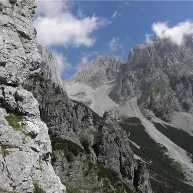 An impressive mountain landscape with steep rocks and high peaks. The sky is partly cloudy and displays a mix of blue and gray light.